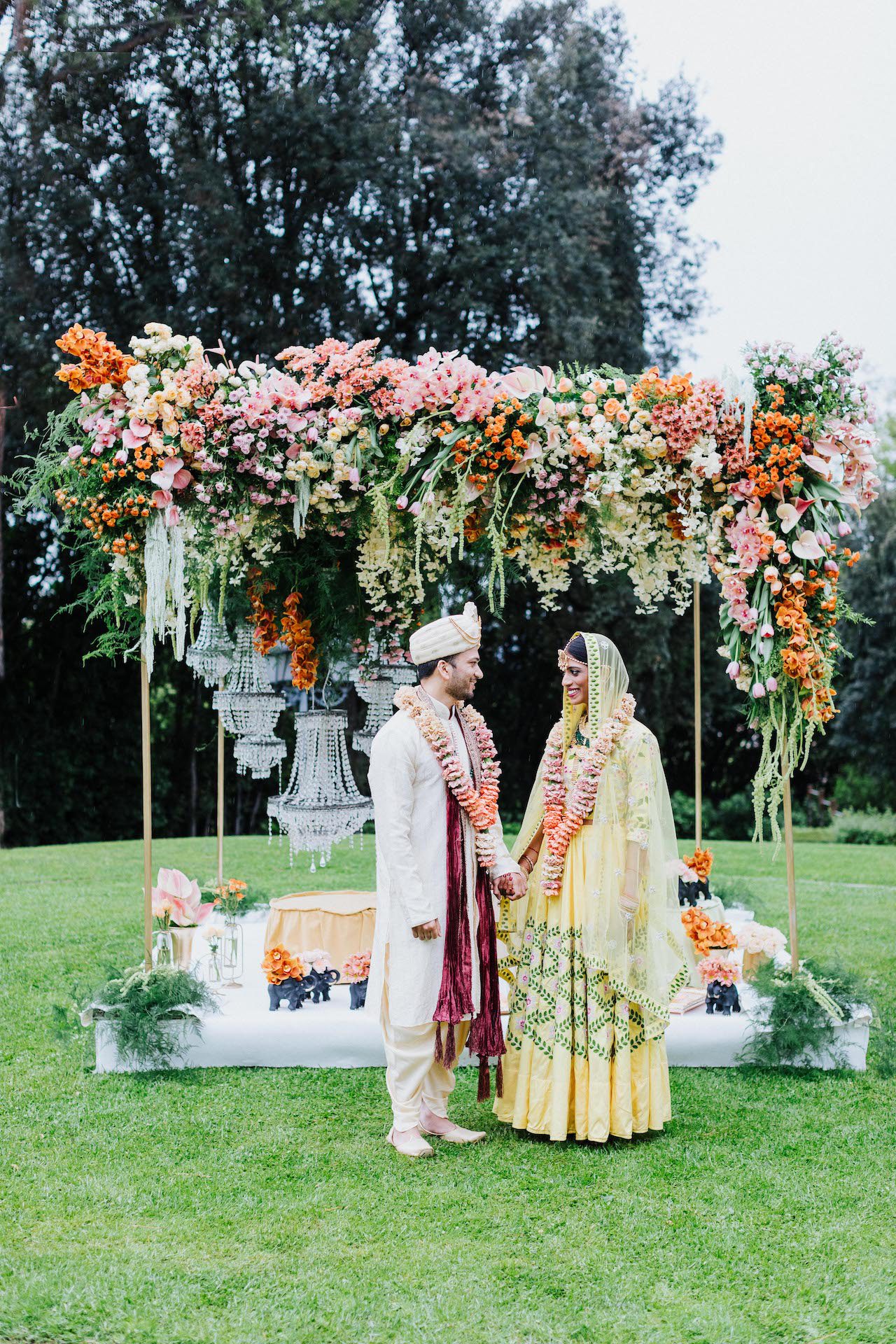 Coppia di sposi indiani davanti al baldacchino Mandap di fiori