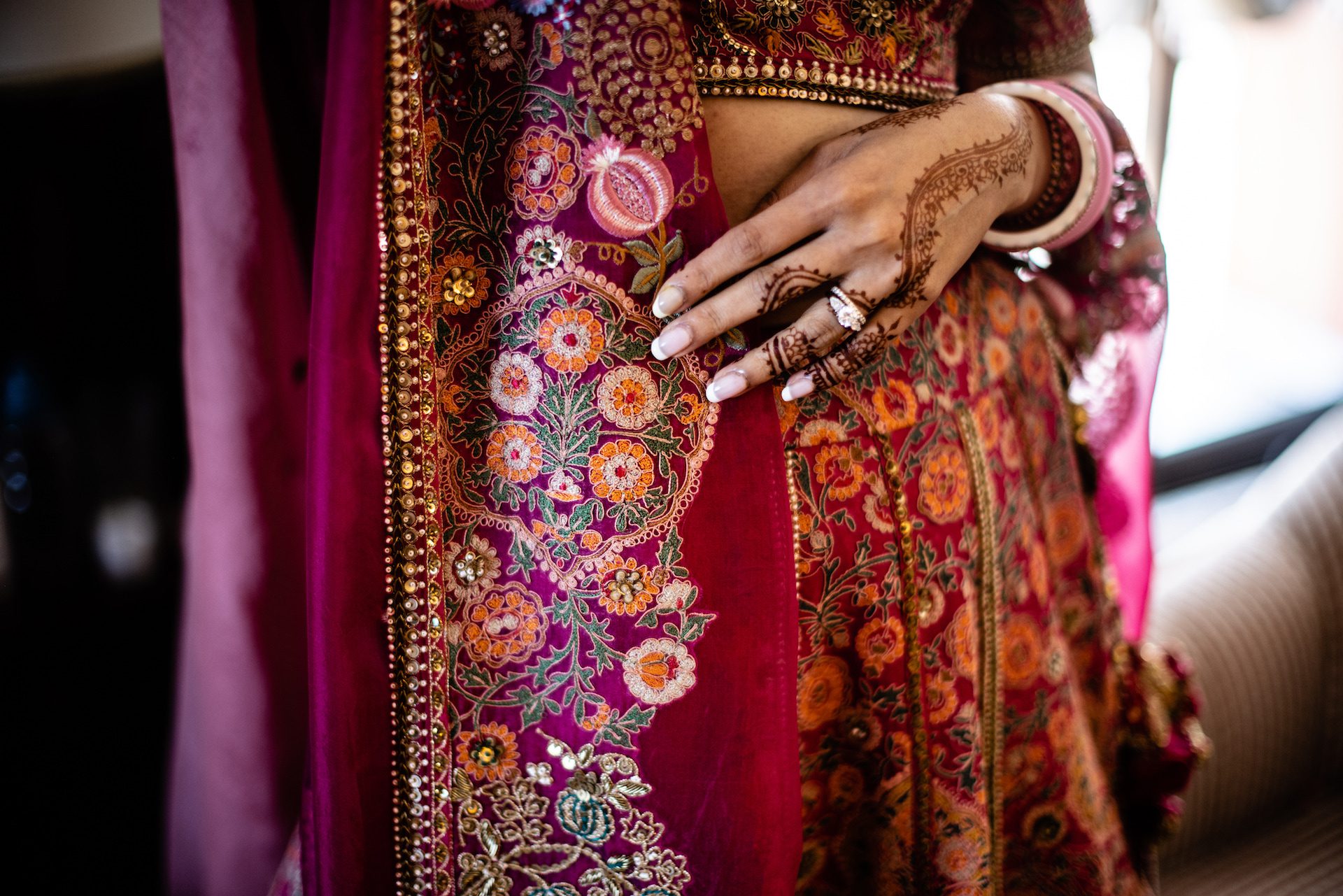 Il dettaglio della mano di una sposa indiana decorata con henne e dell'abito tradizionale delle nozze, con colori accesi dall'arancio al rosso